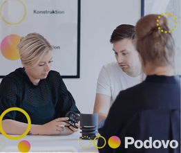 Tre personer taler ved et bord med en bærbar computer. Plakat med cirkler i baggrunden.