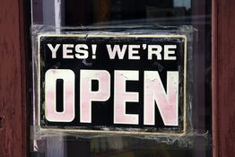 Schild an Tür mit der Aufschrift "YES! WE'RE OPEN" in schwarz-weißem Design.