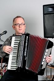 Mann mit Brille spielt Akkordeon vor Mikrofon und mehreren Lautsprechern.