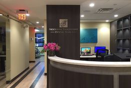 Dental office reception with a curved desk, flowers, and computer; sign reads "Progressive Dental."