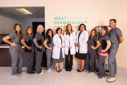 A group of dermatology staff in uniforms and white coats, posing inside an office hallway.