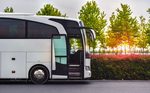 Ein Reisebus/Shuttle steht an einer Straße, wo im Hintergrund die Sonne hinter den Bäumen untergeht.