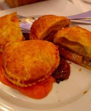 Empanadas doradas sobre salsa naranja en un plato blanco, con cuchillo y tenedor al fondo.