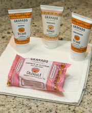 Três tubos de cosméticos e um sabonete Granado sobre toalhas brancas em superfície de pedra.