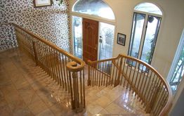 Curved wooden staircase with floral wallpaper and tiled floor leading to a wooden front door.