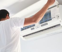 Persona reparando un aire acondicionado en la pared.