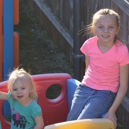 Two children playing on colorful outdoor playground equipment, smiling in sunlight.