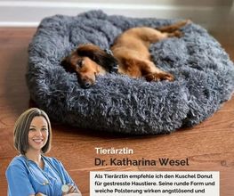 Hund liegt auf grauem, flauschigem Kissen, darunter Werbung für beruhigendes Haustierbett.