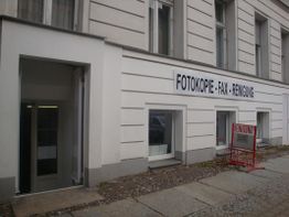 Außenansicht eines Geschäfts mit Schild: "Fotokopie - Fax - Reinigung" an der Wand.