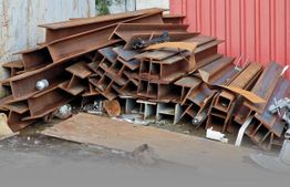 Stapel rostiger Stahlträger vor roter Wand.