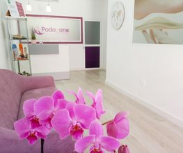Sala de espera moderna con sofá lila y orquídeas rosas. Cartel: "Podo One".