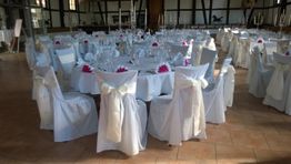 Gedeckter Hochzeitssaal mit runden Tischen und weißen Stühlen, dekoriert mit rosa Blumen.