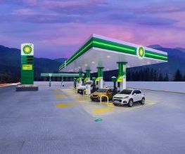 Estación de servicio iluminada al atardecer con autos repostando en un entorno montañoso.