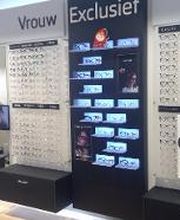 Wand met brillen op displays, onderverdeeld in "Vrouw" en "Exclusief". Diverse stijlen en prijzen.