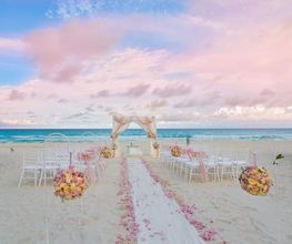 Boda en la playa al atardecer con sillas y flores rosa, y un altar frente al mar.