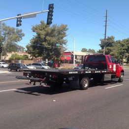 Red tow truck on a city street with trees and traffic lights in the background.