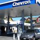 Auto tankt bij Chevron-benzinestation met meerdere pompen en huizen op de achtergrond.