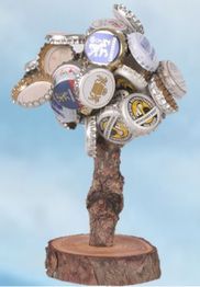 Skulptur aus Flaschenverschlüssen auf Holzstamm, vor blauem Hintergrund.