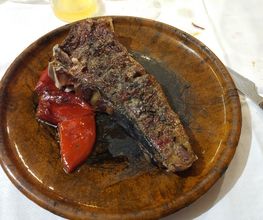 Asado en plato de cerámica con pimientos rojos asados. Cuchillo a la derecha.