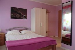 Schlafzimmer mit lila Wänden, Doppelbett, Kleiderschrank, Spiegel und Stadtbild an der Wand.