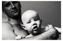 Ein Mann hält ein Baby im Arm. Das Baby schaut neugierig in die Kamera. Schwarz-Weiß-Foto.