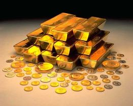 Goldbarren und Münzen sind übereinander gestapelt und leuchten auf einem dunklen Hintergrund.