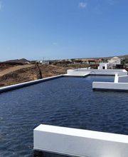 Techo inundado con agua frente a un paisaje desértico y casas, bajo un cielo azul claro.