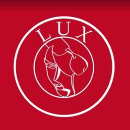 Logo rosso con il marchio "LUX" e un volto stilizzato al centro circondato da un cerchio bianco.