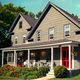 Charming gray house with a red door, porch, and garden full of flowers under a clear sky.