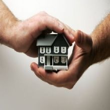 Hands gently holding a small model house, symbolizing protection and care.