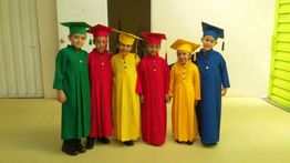 Niños en batas de graduación de colores: verde, rojo, amarillo y azul, sonríen juntos.