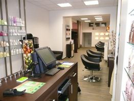 Friseursalon mit vier schwarzen Stühlen, Verkaufstheke mit Computer, Regale mit Produkten.
