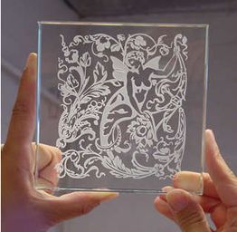 Hands holding etched glass with a fairy and floral design, showing intricate details.