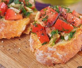 Bruschetta con pomodori freschi, cipolla e erbe su tagliere di legno.