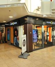 Winkelcentrum met glazen gevel en kledingwinkel links, verlichte ingang en posters in etalage.