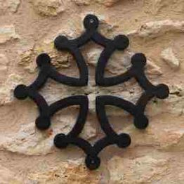 Motif noir sur mur en pierre beige, ressemble à une croix occitane stylisée.