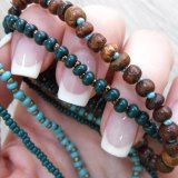 Nahaufnahme von perlenbesetzten Armbändern in einer Hand mit langen, gepflegten Fingernägeln.