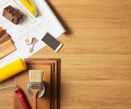Wooden desk with blueprint, paint tools, samples, and a smartphone.