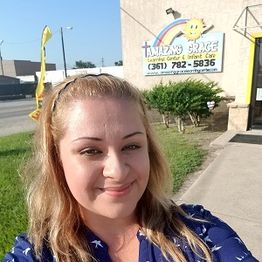 Woman smiling in front of "Amazing Grace" childcare with a rainbow and sun on the wall.