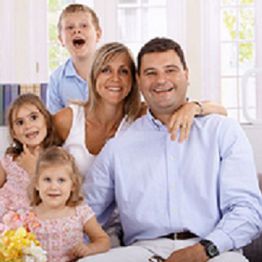 Smiling family of five, with parents and three children, sitting together in a bright room.
