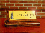 Holzschild mit "Concierge" vor Ziegelwand auf rotem Tisch.