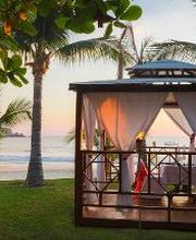 Pérgola junto al mar en un atardecer, rodeada de palmeras y césped verde.