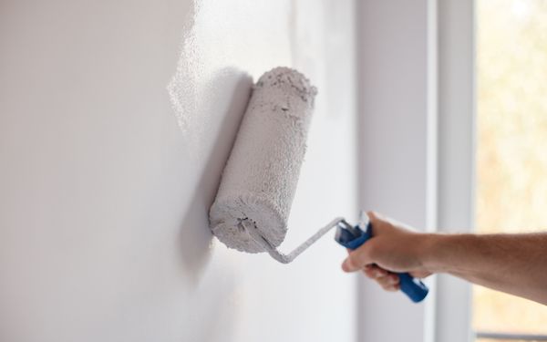 Ein Maler streicht eine Wand mit weißer Engiesparfarbe.