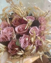 Ramo de rosas rosadas y hierbas secas envuelto en celofán transparente.