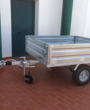 Rimorchio metallico su ruote, parcheggiato su pavimento in piastrelle rosse accanto a una porta verde.