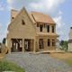 A two-story house under construction with a wooden frame, against a partly cloudy sky.