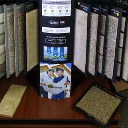 Carpet samples displayed on a stand with labels and promotional material on a wooden table.
