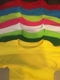 Seis camisetas de colores: rojo, azul, amarillo, rosa, verde y blanco, apiladas ordenadamente.
