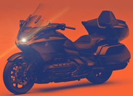 Moto de tourisme noire sur fond orange, éclairée par un phare avant allumé.