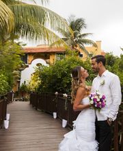Pareja de novios sonríe en un puente rodeado de vegetación, con palmeras al fondo.